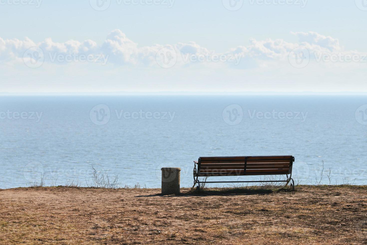 tömma bänk med soptunna på klippa innan hav bakgrund, fredlig tyst plats för tänkande ensam foto