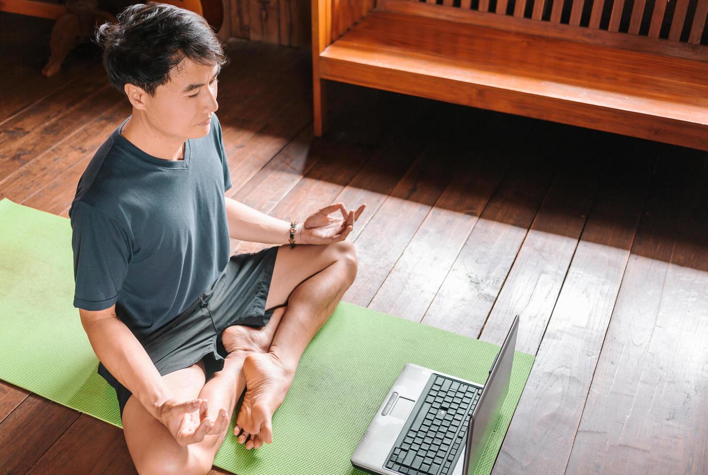 ung asiatisk man tränare internet video uppkopplad Träning yoga instruktör modern bärbar dator skärm meditera sukhasana hållning koppla av andas lätt sittplats utgör Gym friska livsstil på Hem begrepp. foto