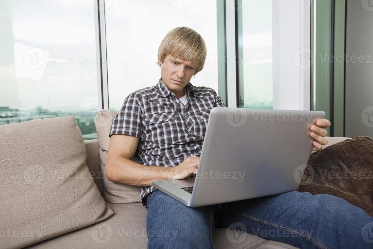 allvarlig mitten av vuxen man använder laptop på soffan hemma foto