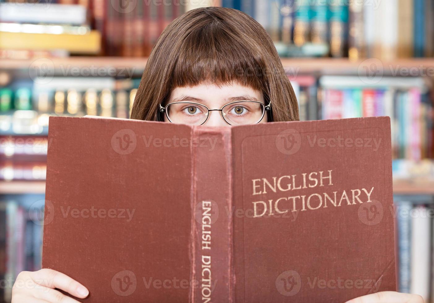 flicka utseende över engelsk ordbok i bibliotek foto