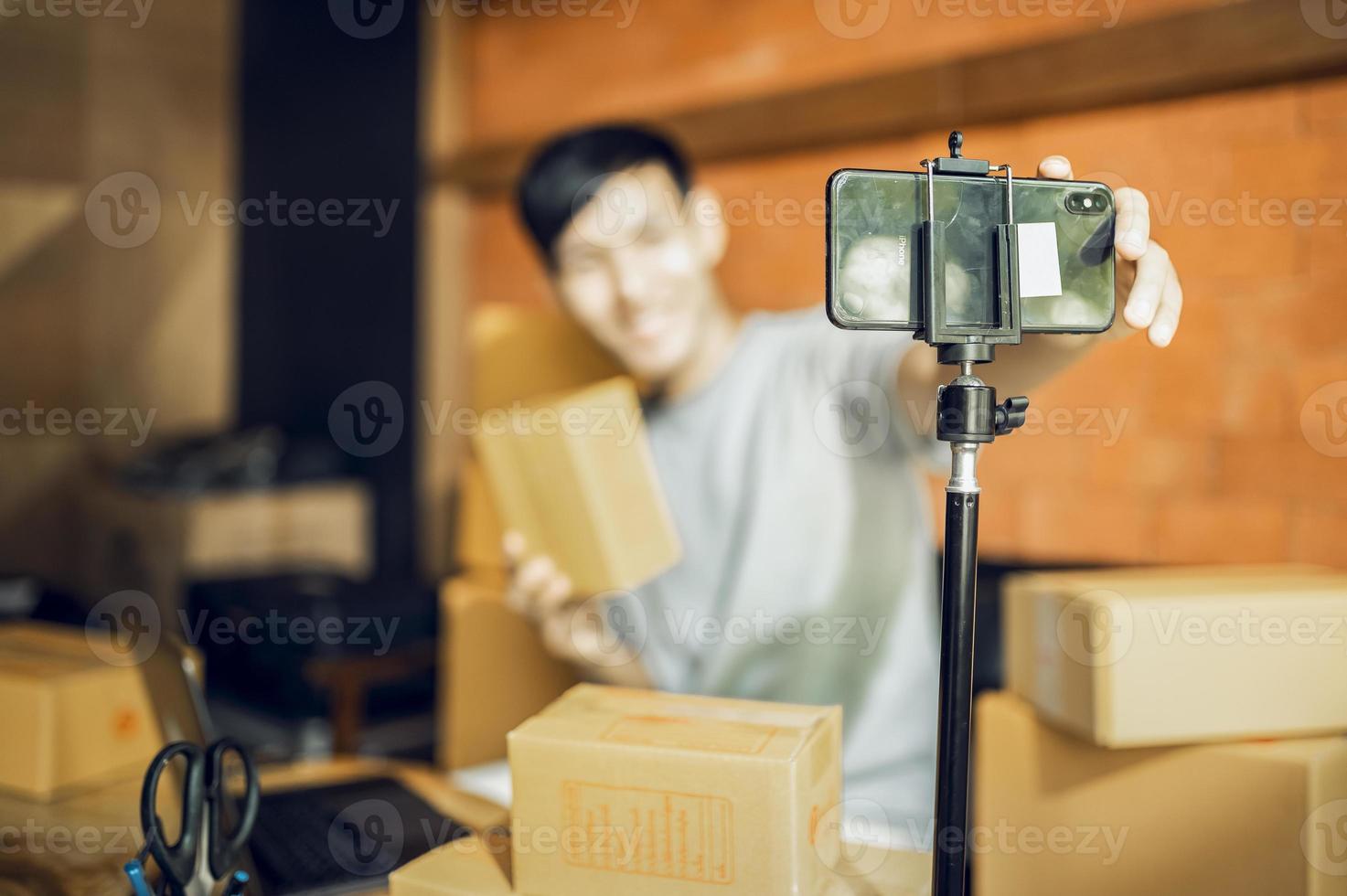 ett asiatisk man användningar en mobil telefon till ta order och visa objekt i en låda den där uppgifter leva strömning video uppkopplad på de Lagra. små företag ägare asiatisk uppkopplad marknadsföra leverans begrepp foto