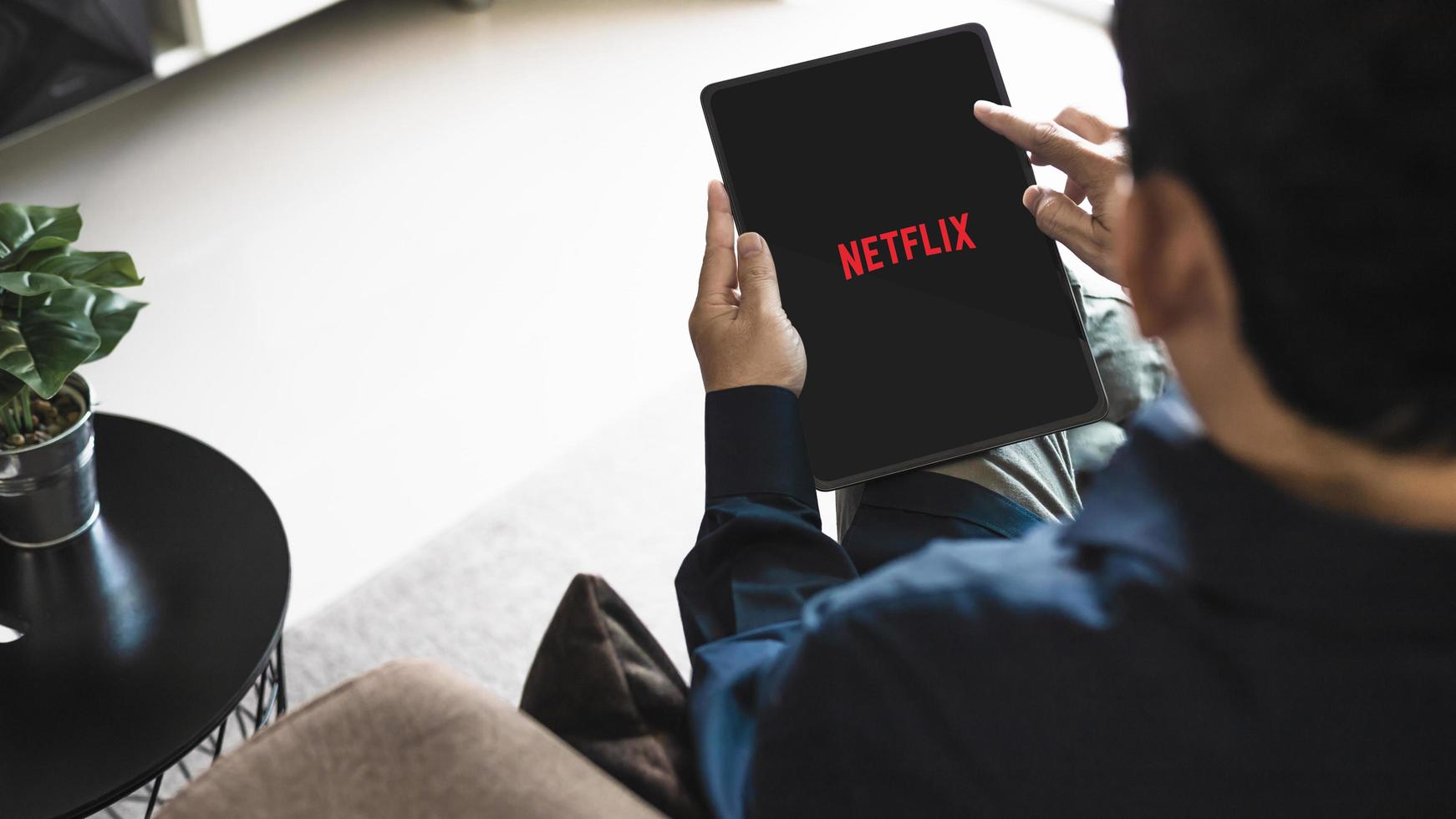 bangkok thailand september 13-2022 manlig använder sig av Netflix Ansökan, strömning bio och TV serier, man innehav ipad på soffa i levande rum på Hem. foto