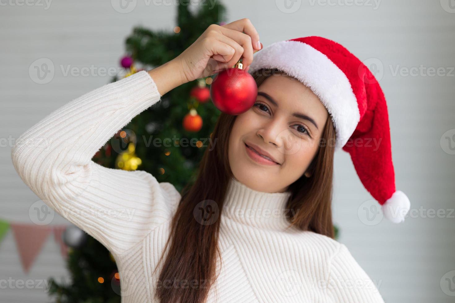 glad jul och Lycklig högtider, skön kvinna innehav röd jul boll till dekorera de jul träd inomhus i de morgon- innan xmas foto