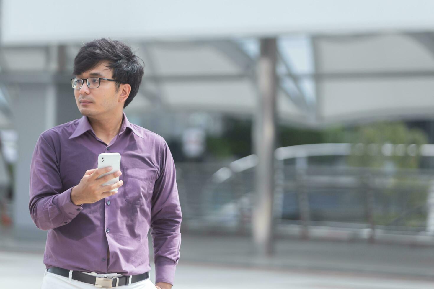 svettas ung asiatisk affärsman ser på meddelanden på mobiltelefon medan gående i de gata. foto