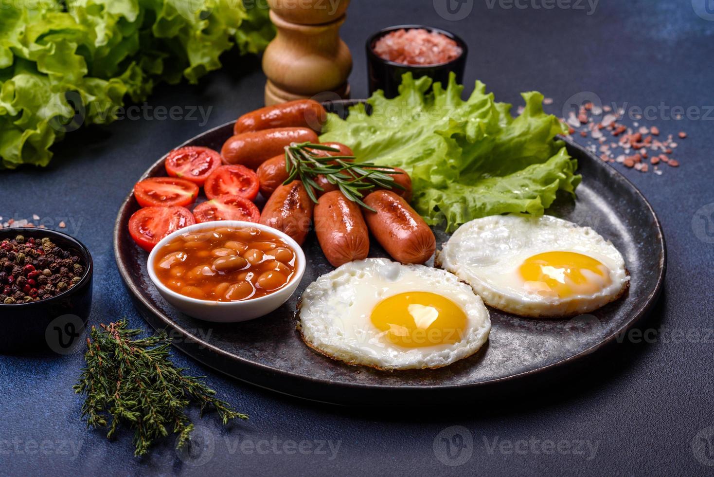 traditionell engelsk frukost med ägg, rostat bröd, korvar, bönor, kryddor och örter på en grå keramisk tallrik foto