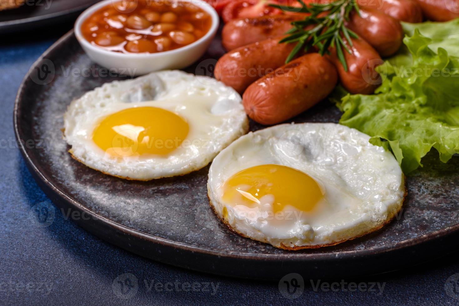 traditionell engelsk frukost med ägg, rostat bröd, korvar, bönor, kryddor och örter på en grå keramisk tallrik foto