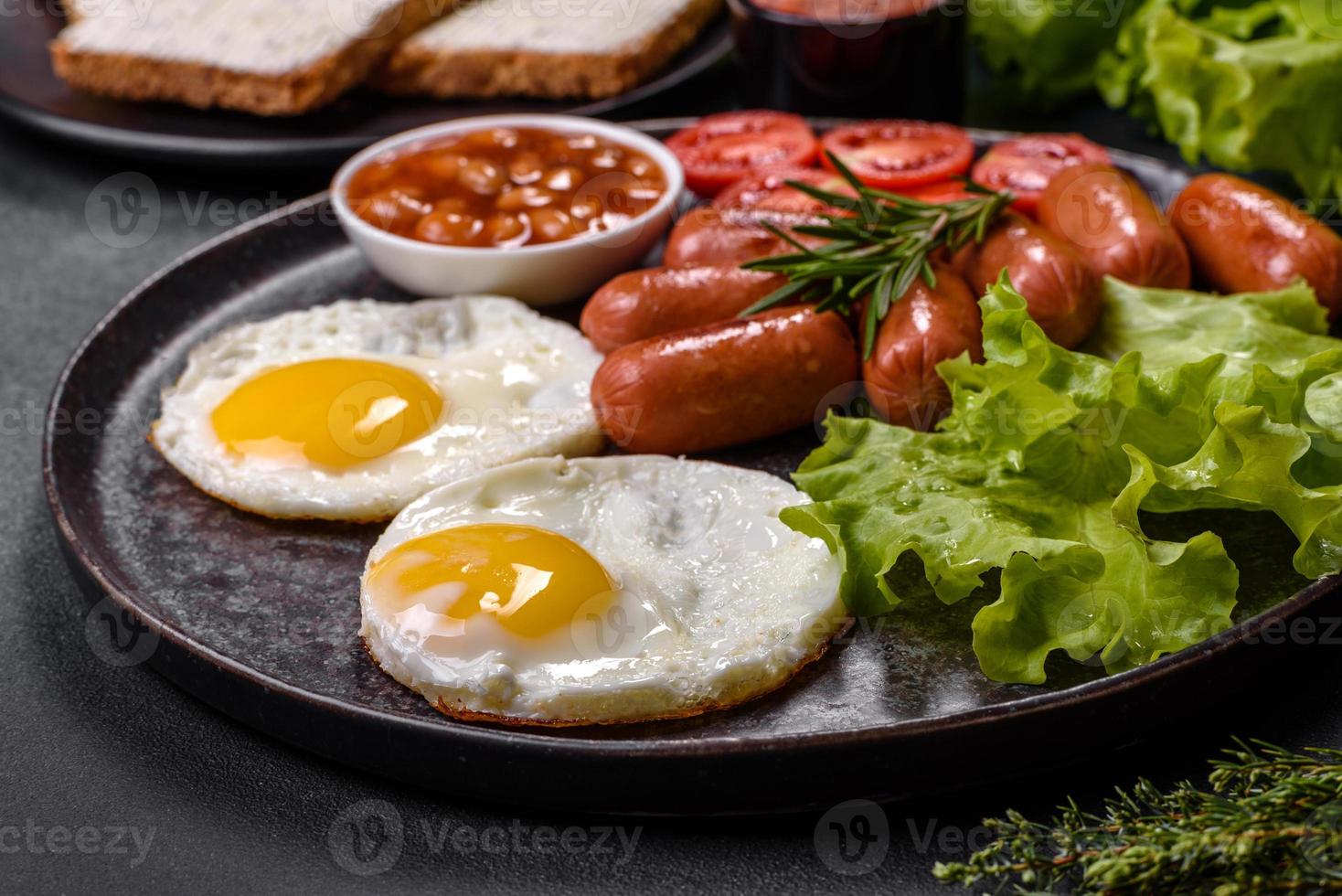 traditionell engelsk frukost med ägg, rostat bröd, korvar, bönor, kryddor och örter på en grå keramisk tallrik foto
