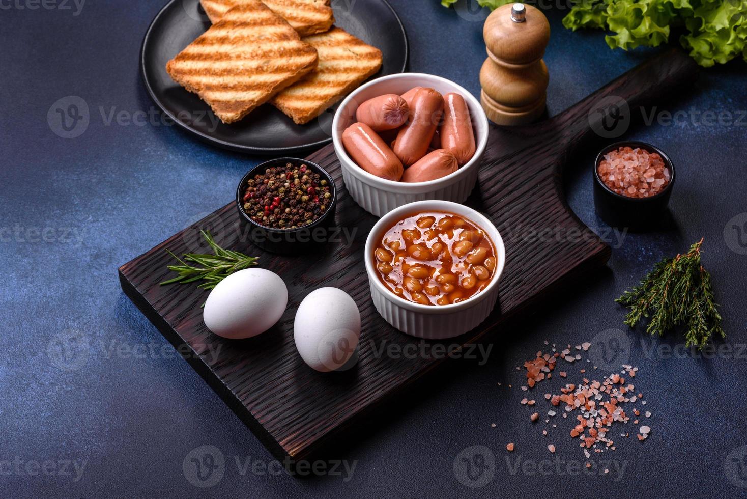 traditionell engelsk frukost med ägg, rostat bröd, korvar, bönor, kryddor och örter på en grå keramisk tallrik foto