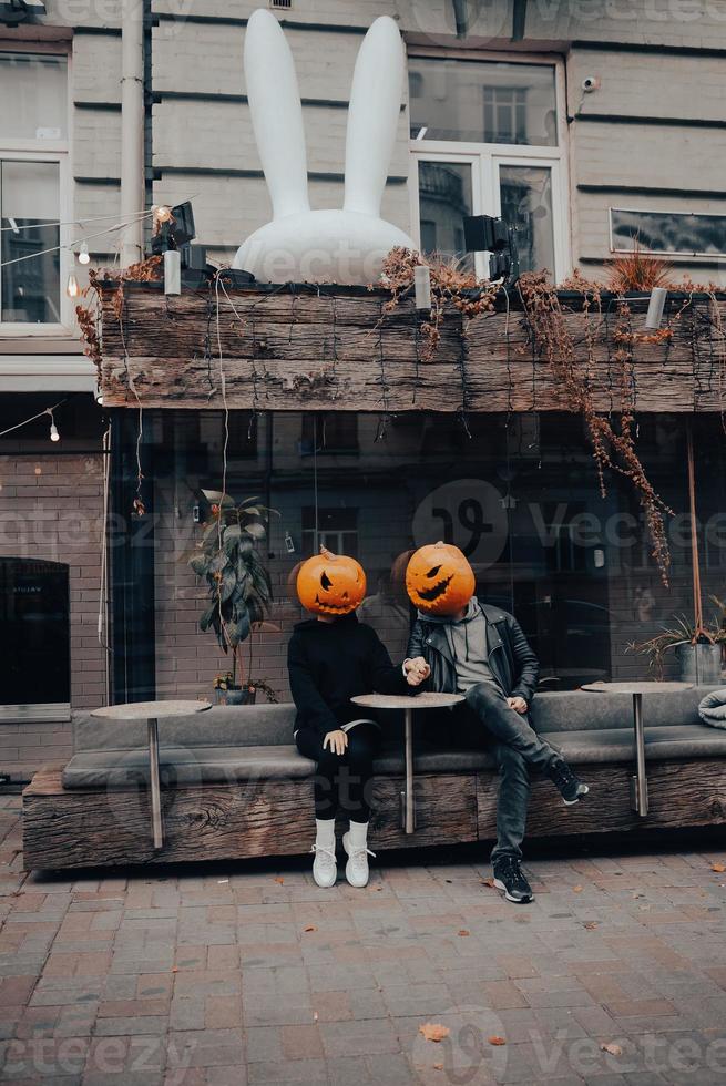 kille och flicka med pumpa huvuden i en gata Kafé innehav händer foto