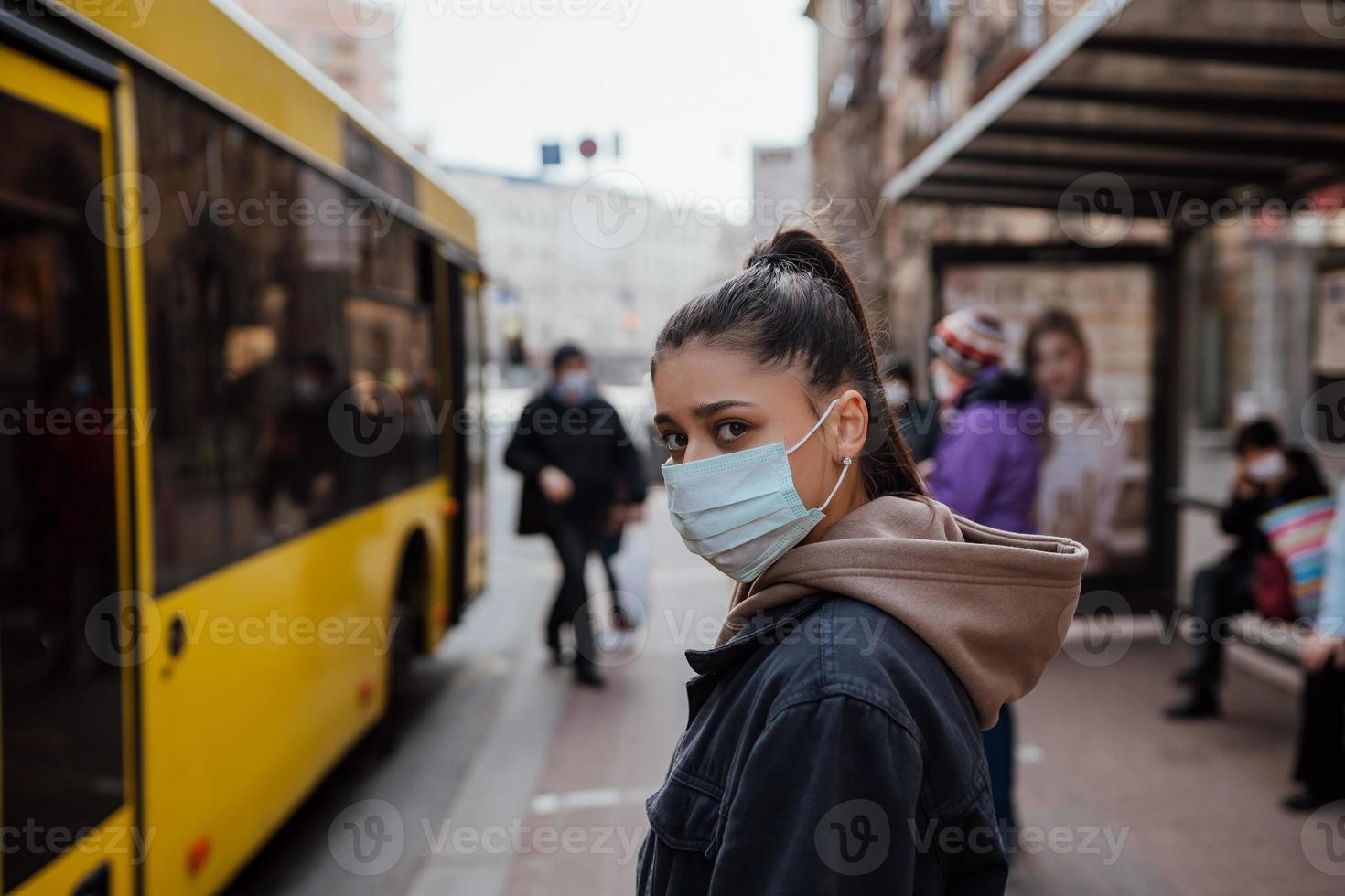 ung kvinna bär kirurgisk mask utomhus- på buss sluta i de gata foto