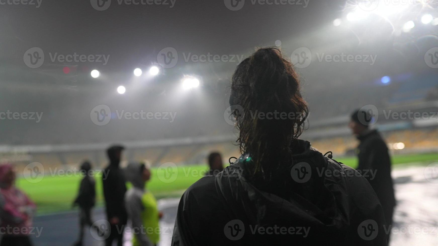 människor gå i för sporter på natt stadion i regnig väder foto