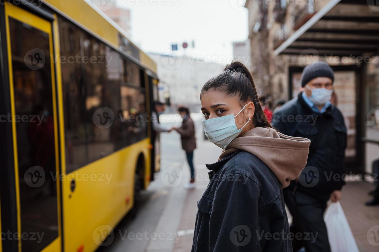 ung kvinna bär kirurgisk mask utomhus- på buss sluta i de gata foto