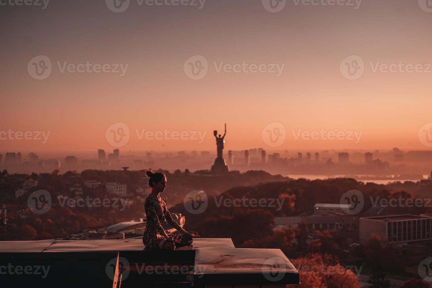 kvinna håller på med yoga på de tak av en skyskrapa i stor stad. foto