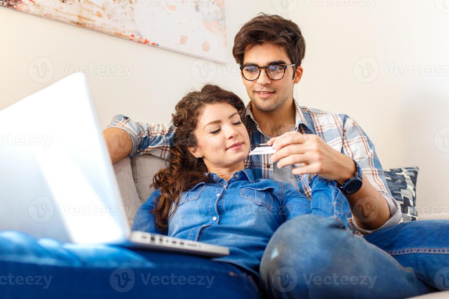 leende unga par som shoppar online via den bärbara datorn i deras hem. foto