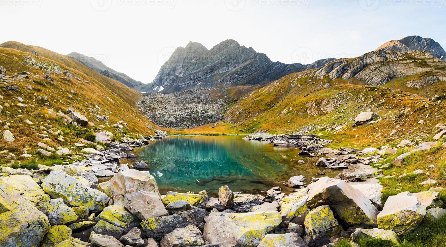 bergen grön sjö med reflektioner och klippig Strand i höst tid. vild natur och lantlig montera dal. falla grå väder regnig moln på himmel. kall sjö, vinter- kommande landskap foto