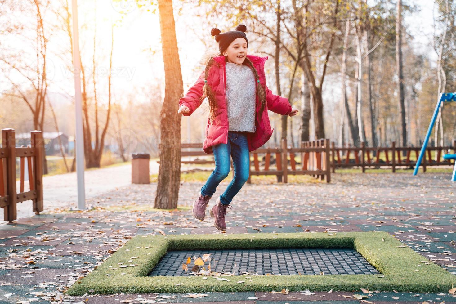 Lycklig skola flicka Hoppar på en små trampolin i de parkera foto