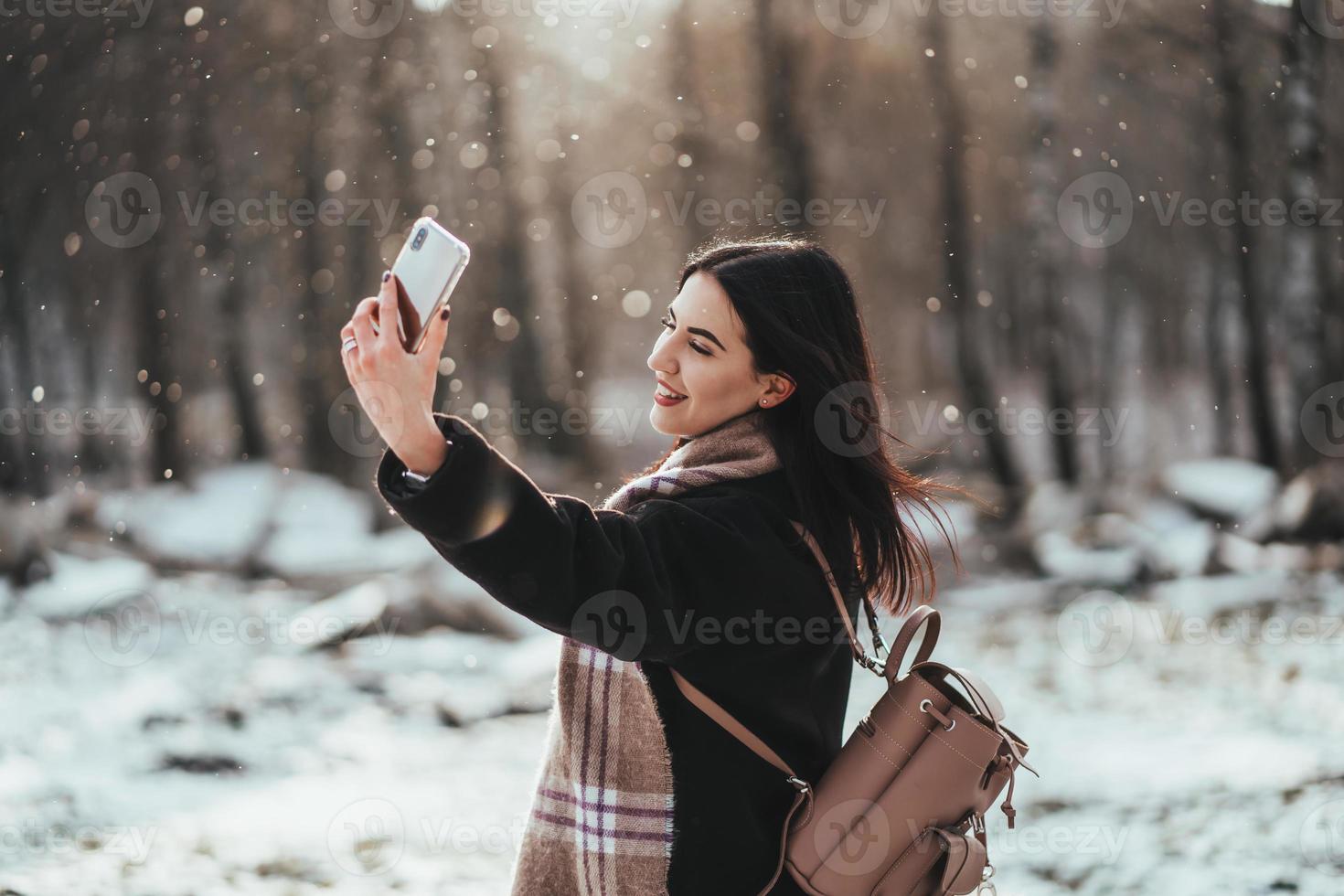 Lycklig leende Tonårs flicka eller ung kvinna tar selfie förbi smartphone i vinter- parkera foto