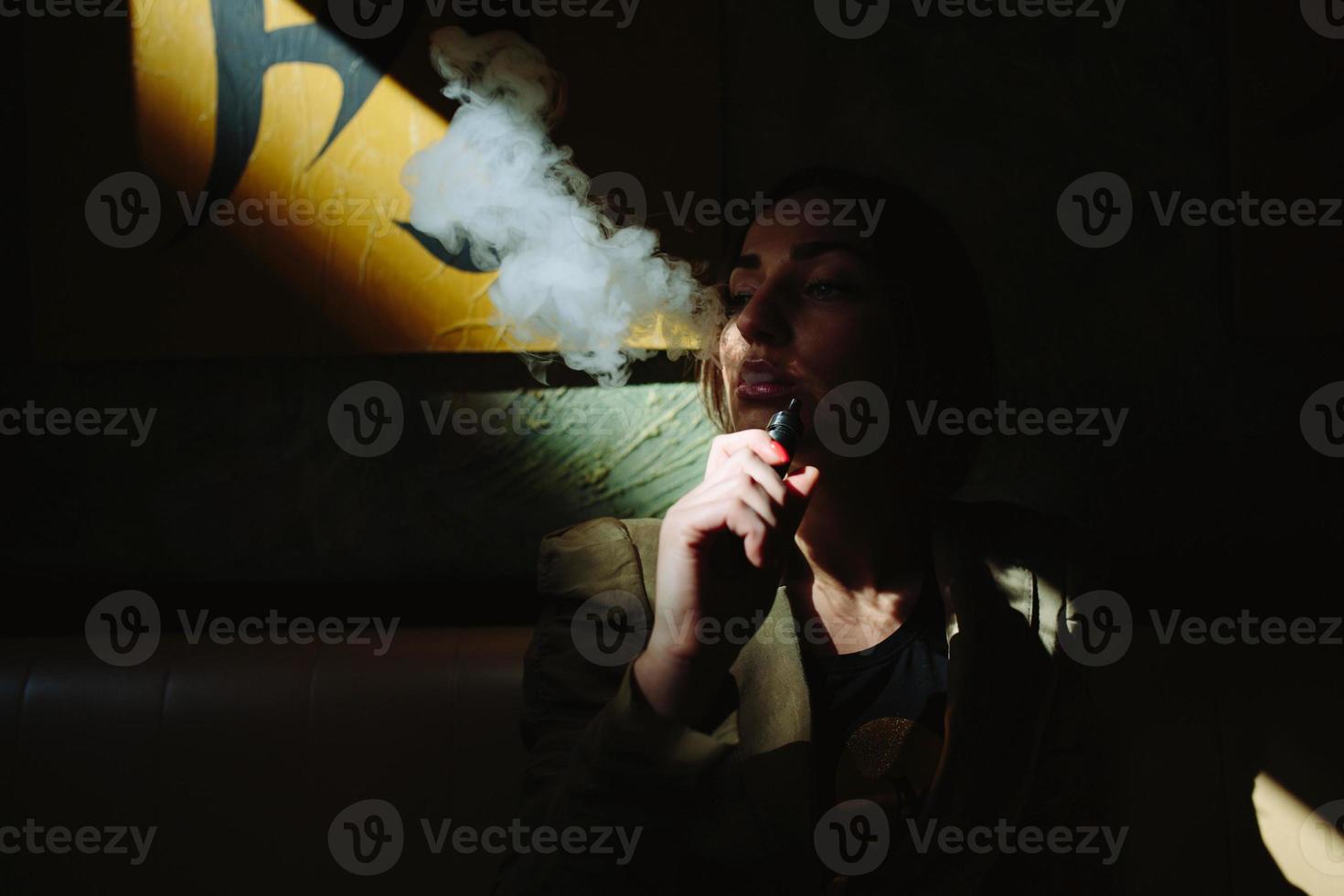 flicka sitter och röker elektronisk cigarett foto
