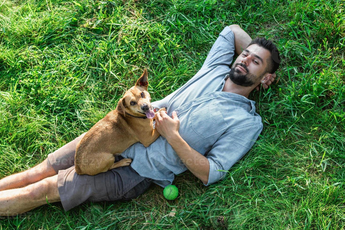 attraktiv europeisk man är vilar på gräs med hans söt liten hund på en sommar solig dag. foto