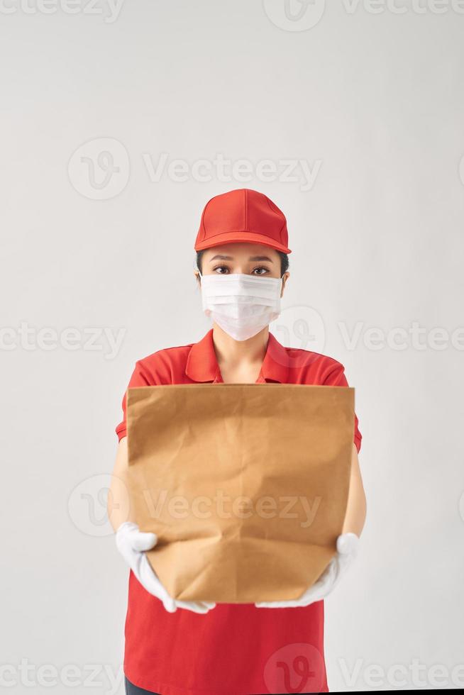 hälsa skydd, säkerhet och pandemi begrepp - leverans kvinna i skyddande ansikte mask med mat i papper väska över rosa bakgrund foto