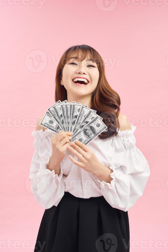 bild av förtjust kvinna bär grundläggande kläder leende och innehav pengar kontanter isolerat över rosa bakgrund foto
