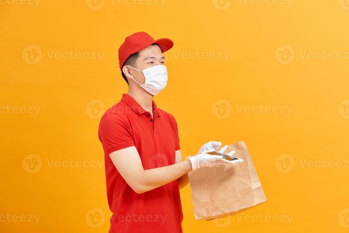 leverans man innehav papper väska med mat på vit bakgrund, mat leverans man i skyddande mask och skyddande handskar foto