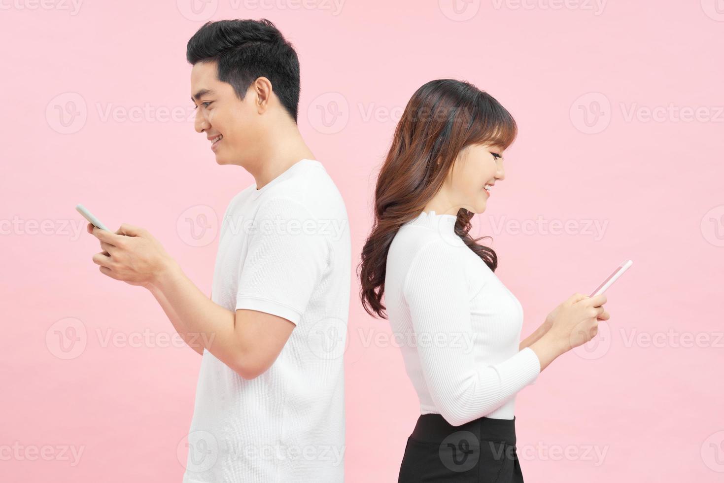 romantisk meddelanden. skön ung kärleksfull par innehav mobil telefoner och stående tillbaka till tillbaka mot rosa bakgrund foto