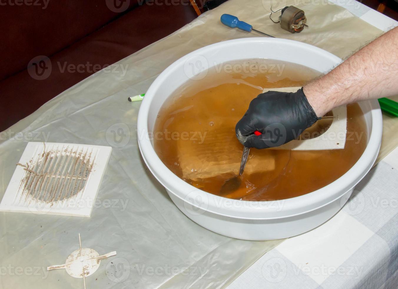 tvättning de plast delar av en mycket smutsig kök uttömma fläkt i ett vattenhaltig lösning av natrium hydroxid. en man Arbetar i skyddande handskar. foto