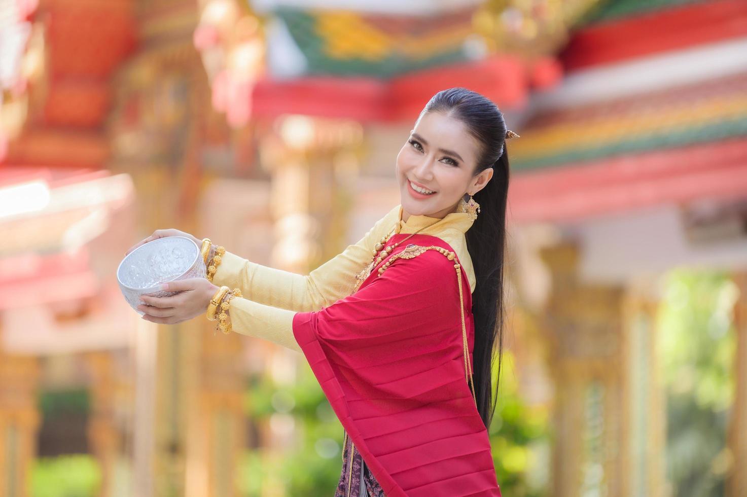 en vacker thailändsk kvinna i thailändsk klänning med guldprydnader håller en kopp vatten för songkran-festivalen eller thailändska nyåret foto