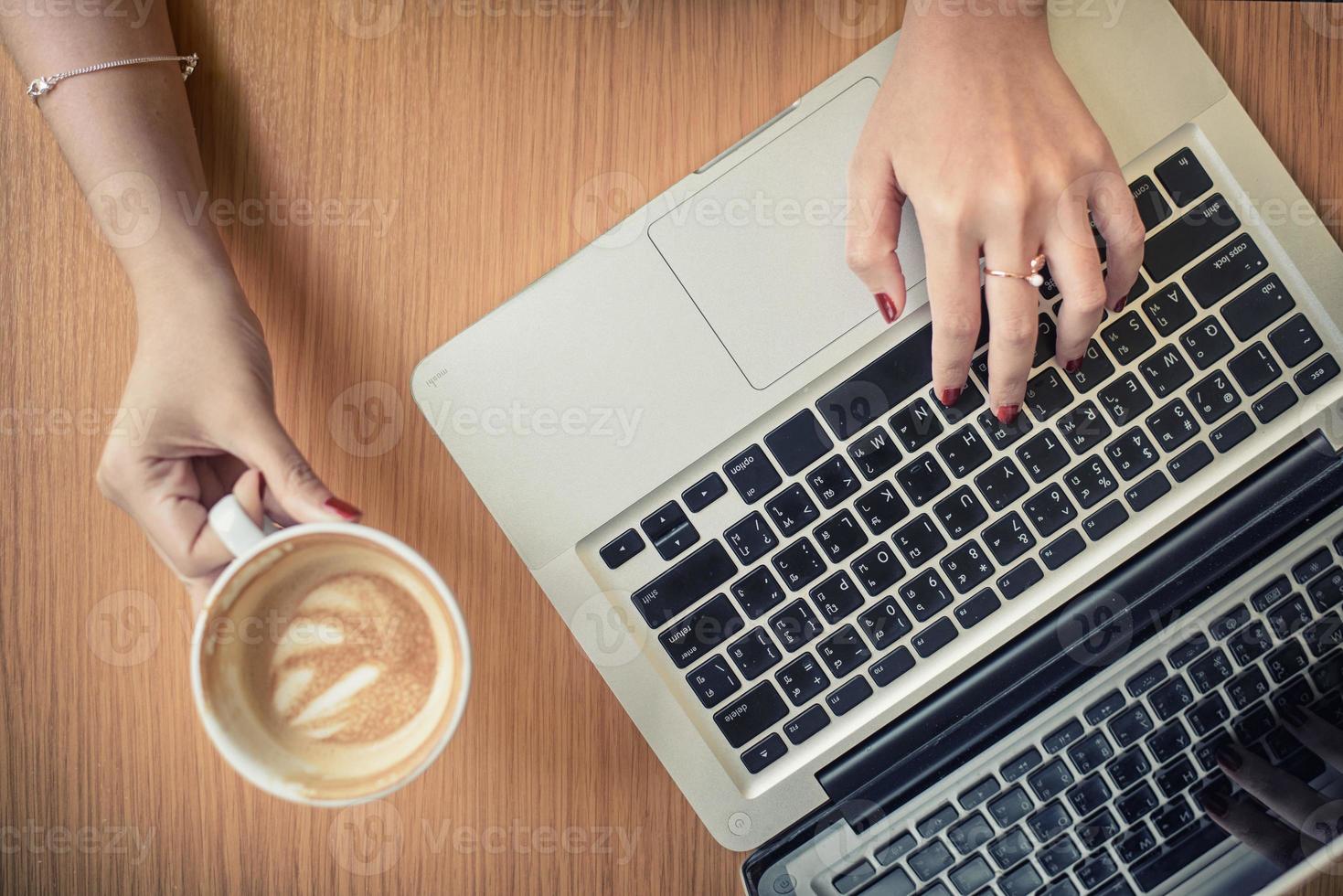bärbar dator och kaffe kopp i flickans händer Sammanträde på en trä- bakgrund foto