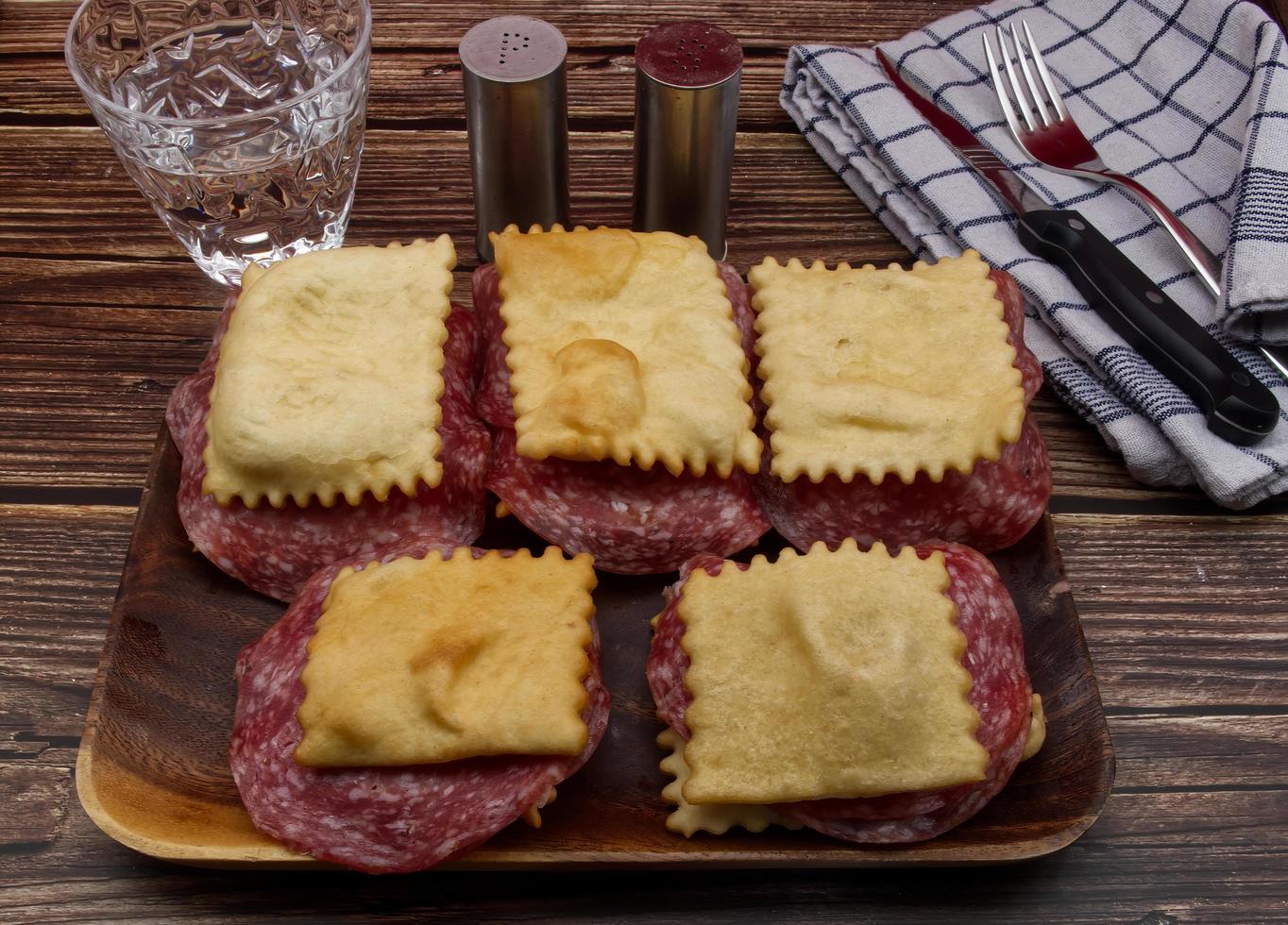 italiensk gnocco fritto med salami på rustik trä- tabell. ersättning för bröd tillverkad med friterad deg. foto