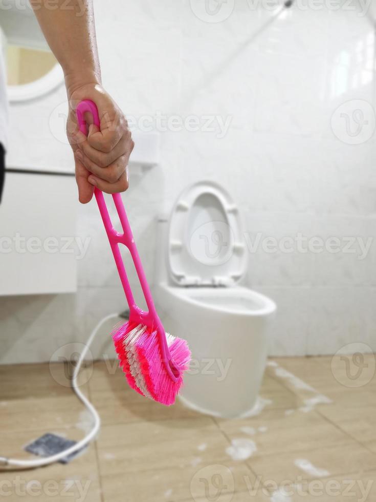 kvinna rengöring toalett med skrubba borsta suddigt badrum foto