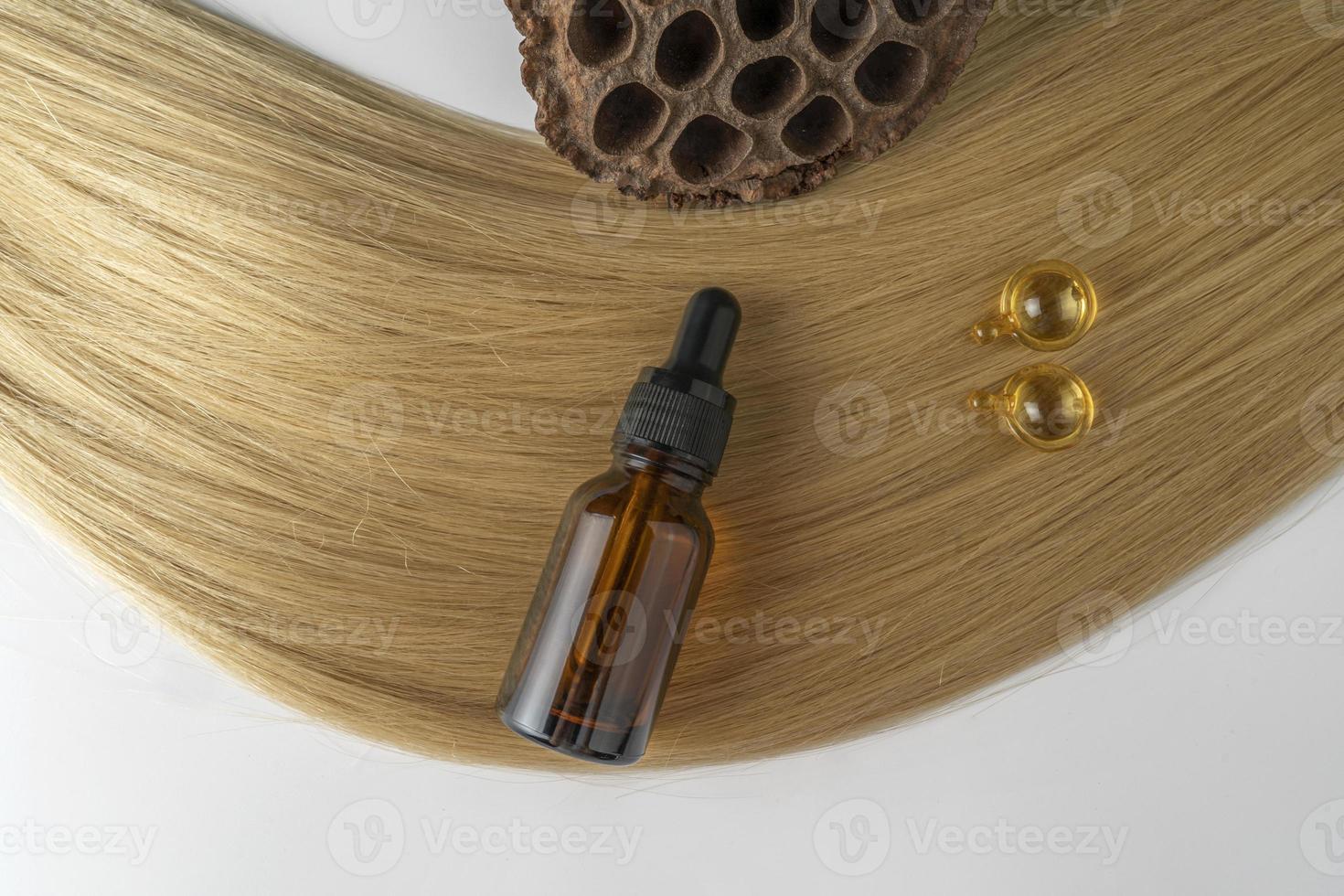 en brun dropper flaska och gyllene kapslar för ansikte vård liggande på en strå av blond hår foto
