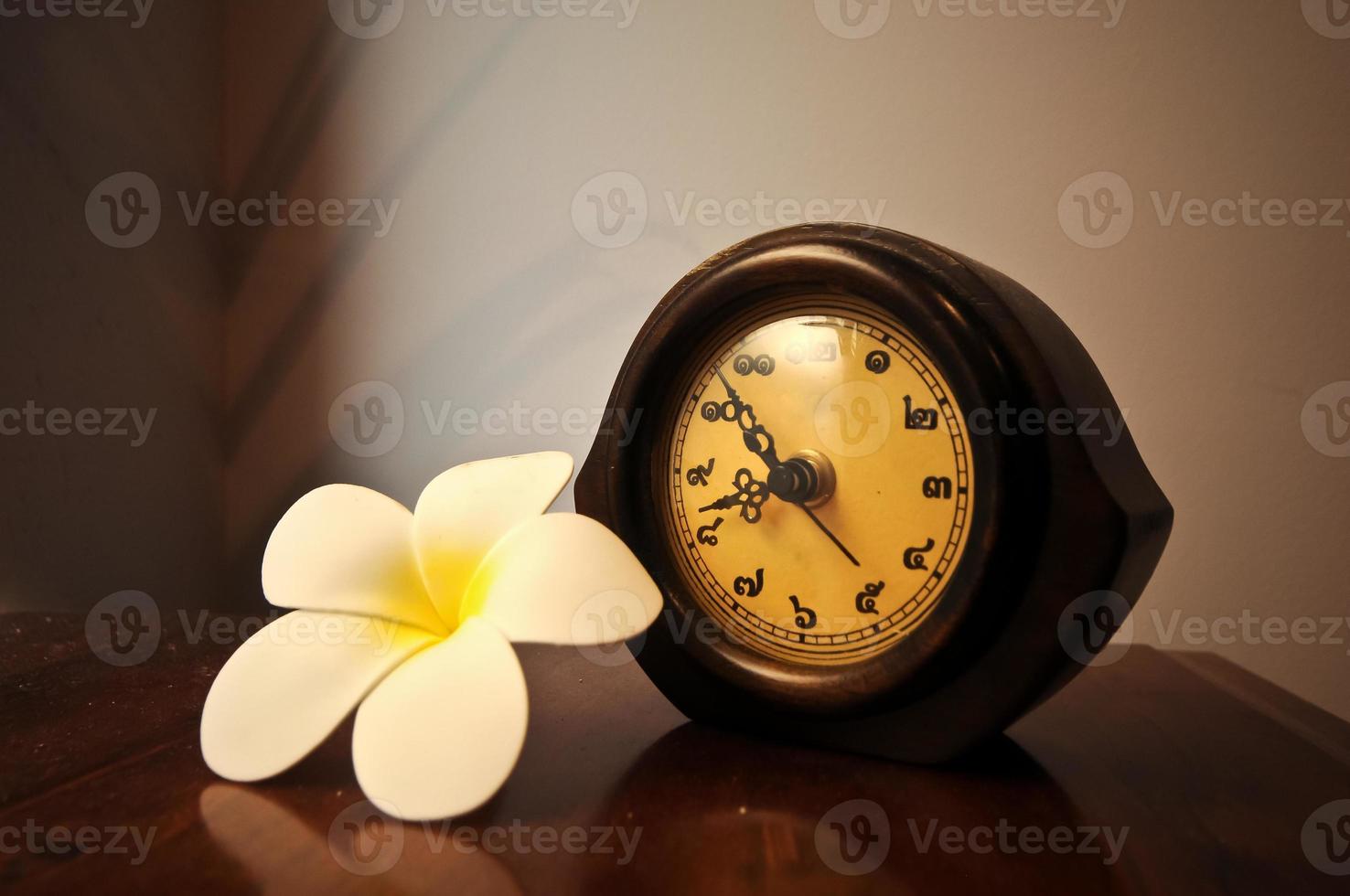 årgång trä- thai skrivbord klocka på en tabell med plumeria blomma foto