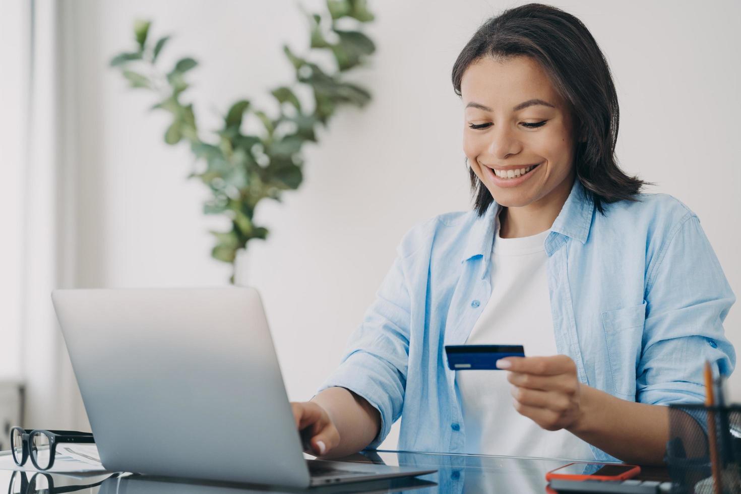 Lycklig latinamerikan kvinna använder sig av kreditera kort. kund är njuter uppkopplad handla med internet bankverksamhet. foto