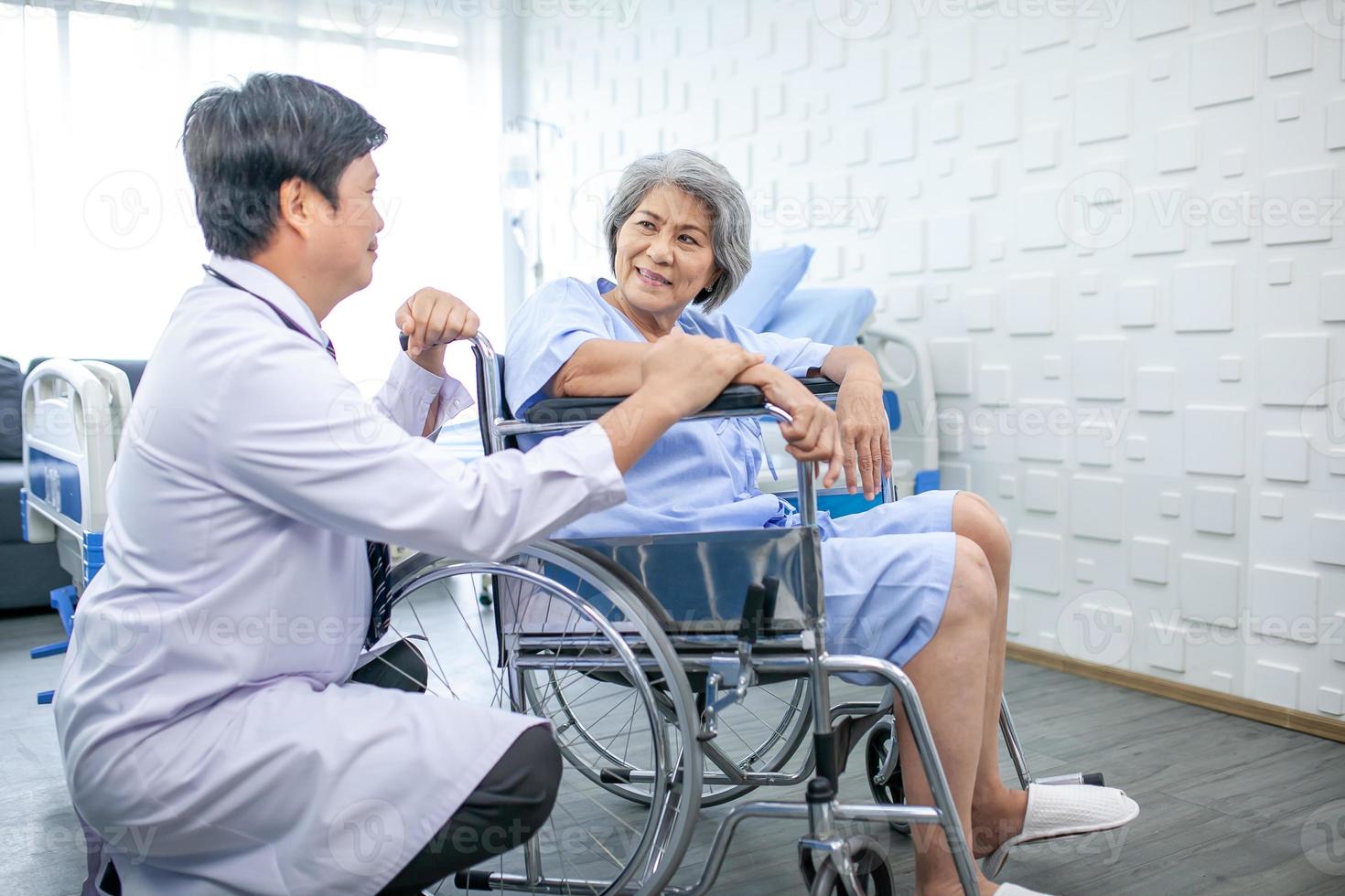 asiatisk läkare stödjande och glädjande upp senior patient i rullstol talande, leende i bekvämlighet på sjukhus. sjukvård och medicin begrepp. foto