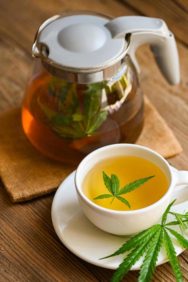 hälsa te med hampa blad växt thc cbd örter mat och medicinsk begrepp, cannabis te ört- på te kopp och kanna med cannabis blad marijuana löv ört på trä- foto
