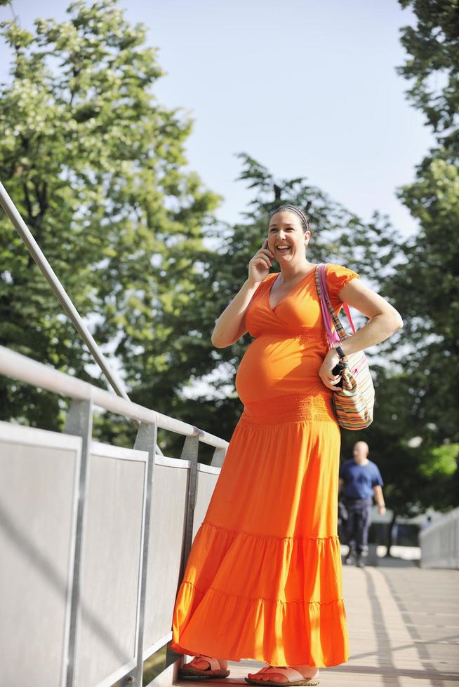 Lycklig gravid kvinna talande förbi mobiltelefon foto