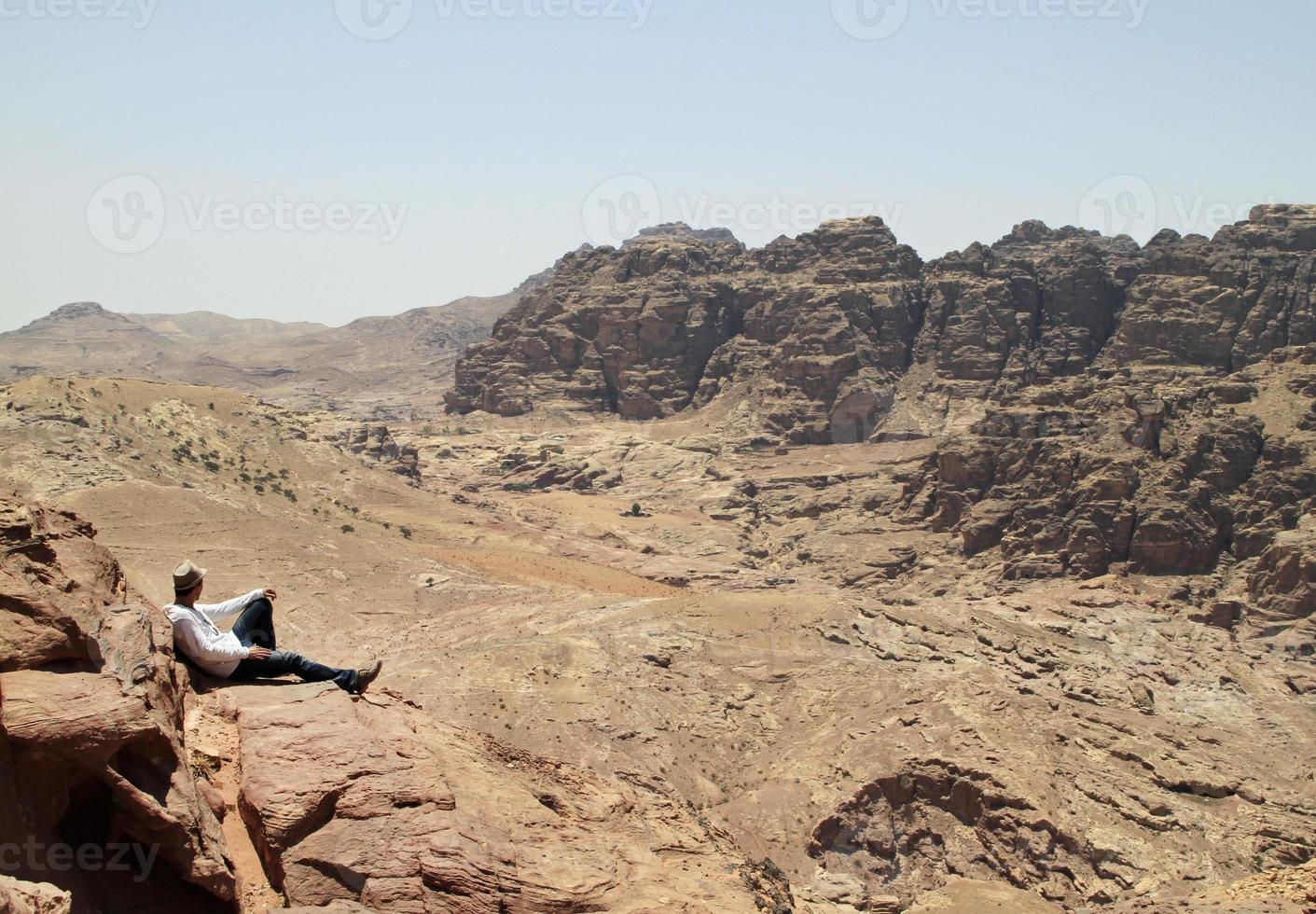 ung man på toppen av en topp med utsikt över en dal i det karga landskapet i petra, jordan foto