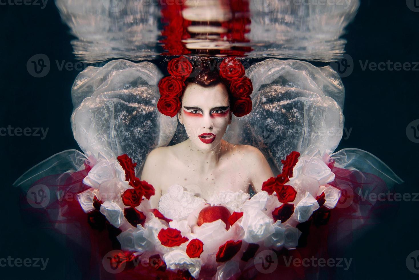 kvinna i klänning tillverkad av vit och röd ro under vattnet. fe- berättelse, konst, mode begrepp foto