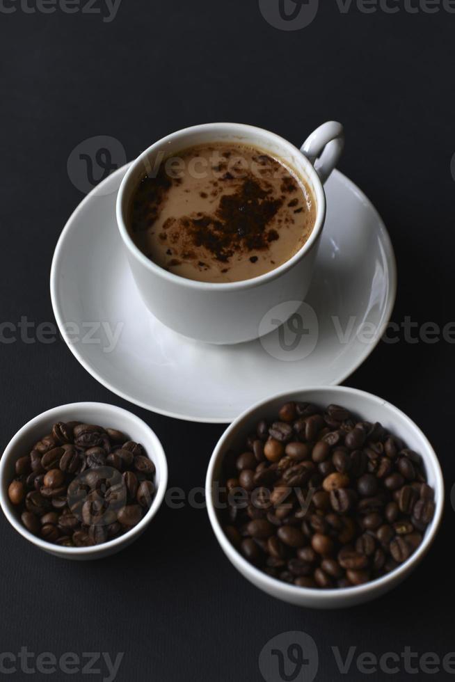 utsökt kaffe i en porslin kopp med en fat och kaffe bönor. kaffe i en kopp och bönor på en svart bakgrund. foto