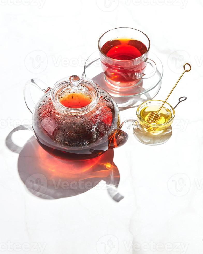 frukt te med äpplen och timjan och honung i glas tekanna och kopp på vit bakgrund med hård skuggor foto