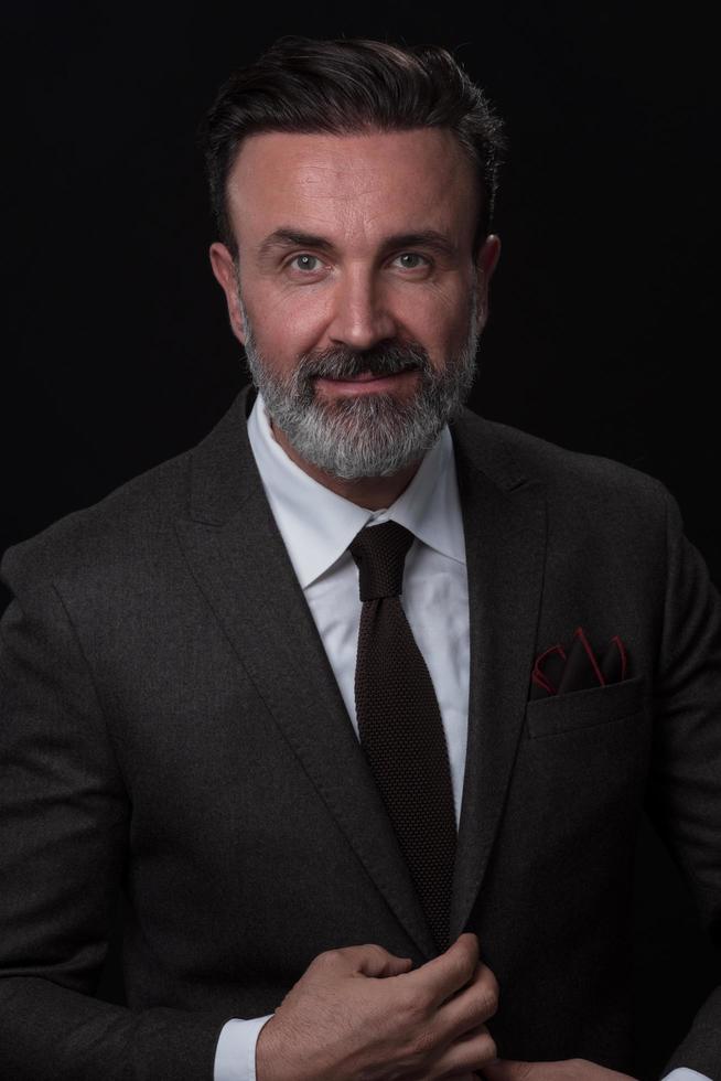 porträtt av en eleganta elegant senior affärsman med en skägg och tillfällig företag kläder i Foto studio isolerat på mörk bakgrund gestikulerar med händer