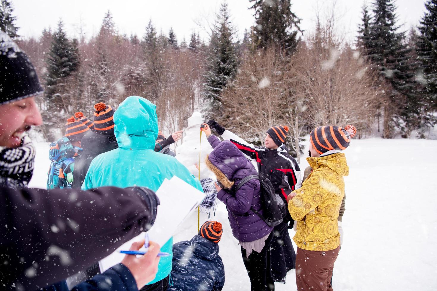 ung människor mätning de höjd av färdiga snögubbe foto