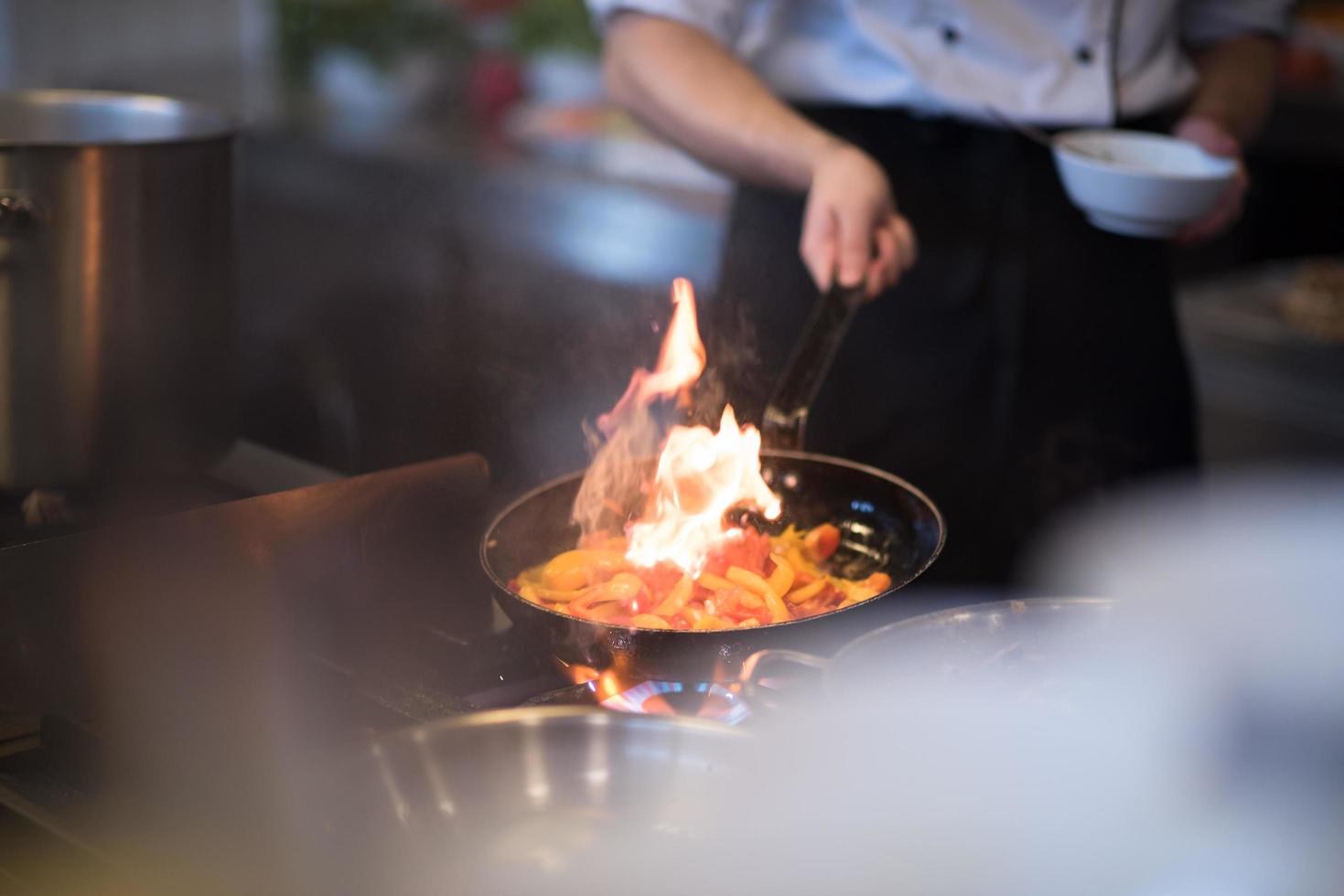 kock håller på med flambe på mat foto