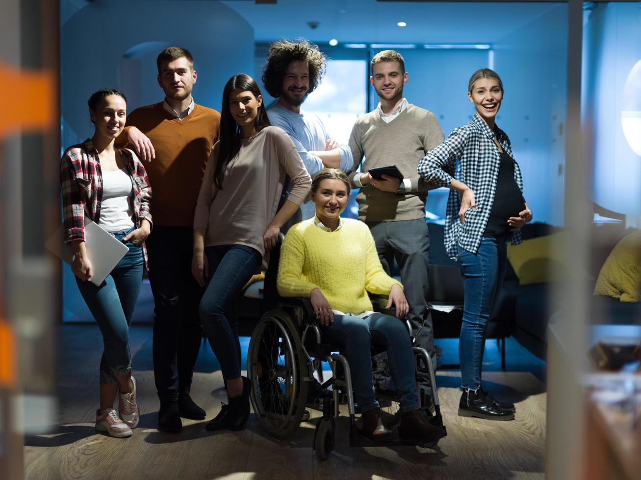 Inaktiverad affärskvinna i en rullstol på de kontor med medarbetare team foto