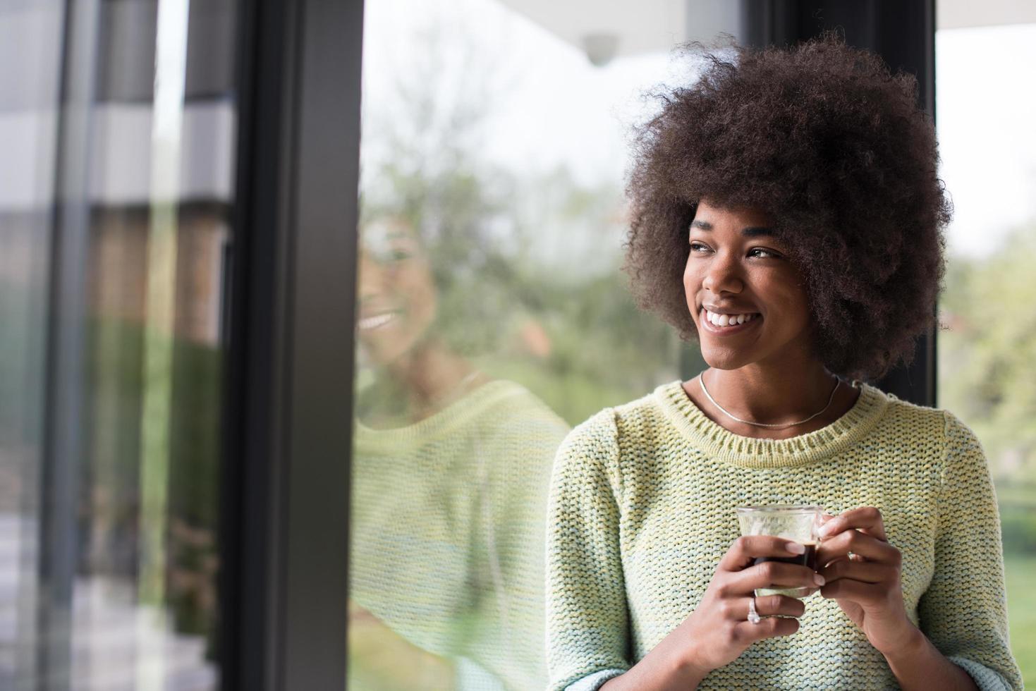 afrikansk amerikan kvinna dricka kaffe ser ut de fönster foto