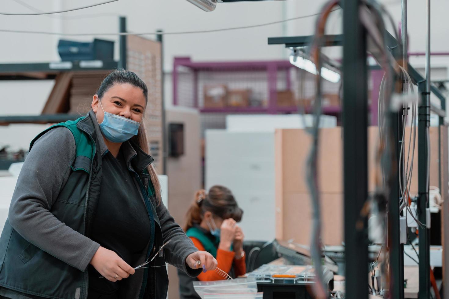 ett fet kvinna Arbetar i en tung metall fabrik, bär en mask på henne ansikte på grund av till en coronavirus pandemi foto