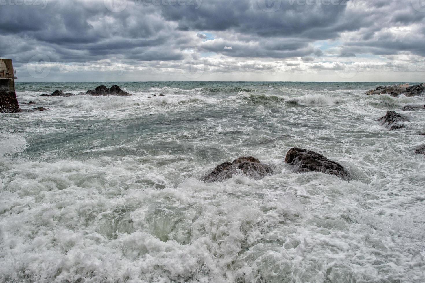 hav i storm på stenar av italiensk by foto