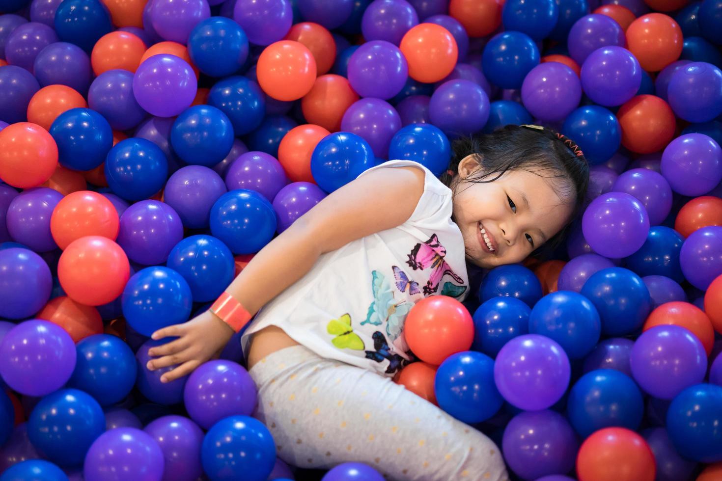 ung asiatisk tjej som spelar i bouncy ball pit foto